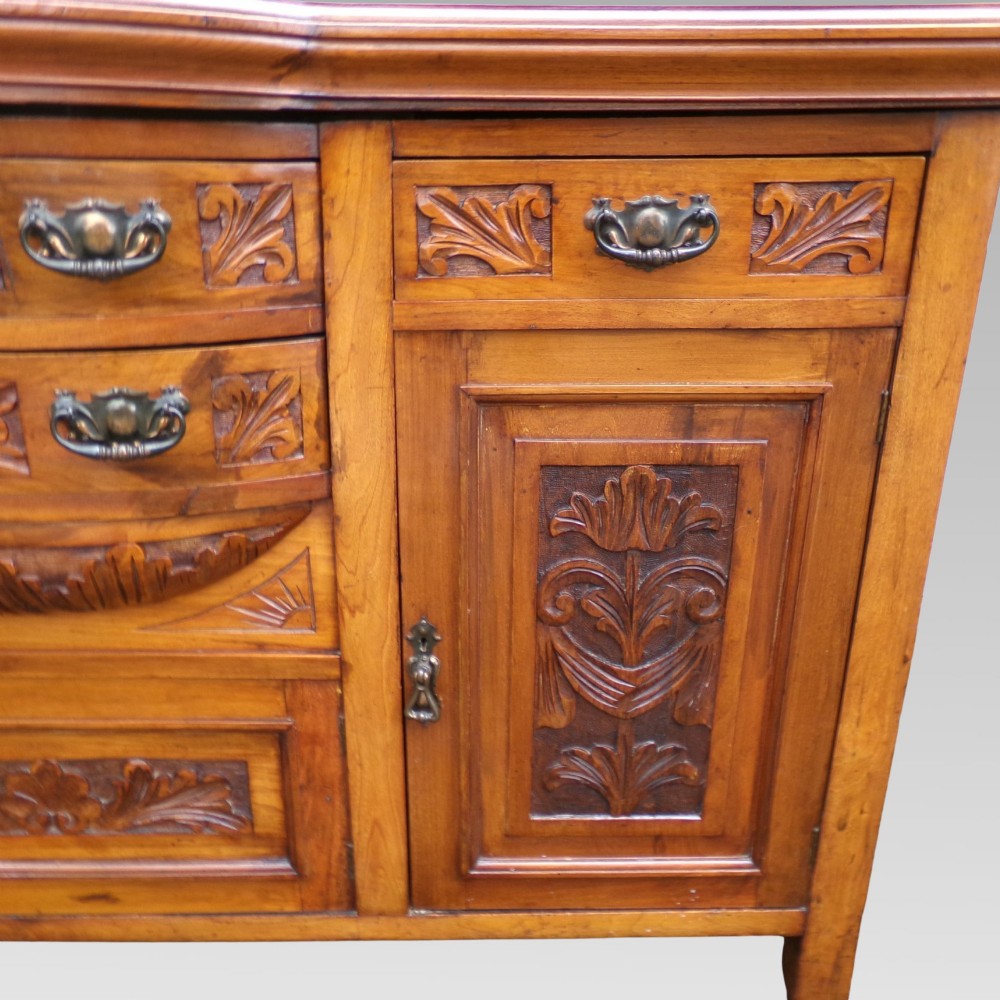 A carved Edwardian mahogany sideboard featuring a bow-front centre section with drawers, flanked by cupboard doors with stylised plant motifs. View VII