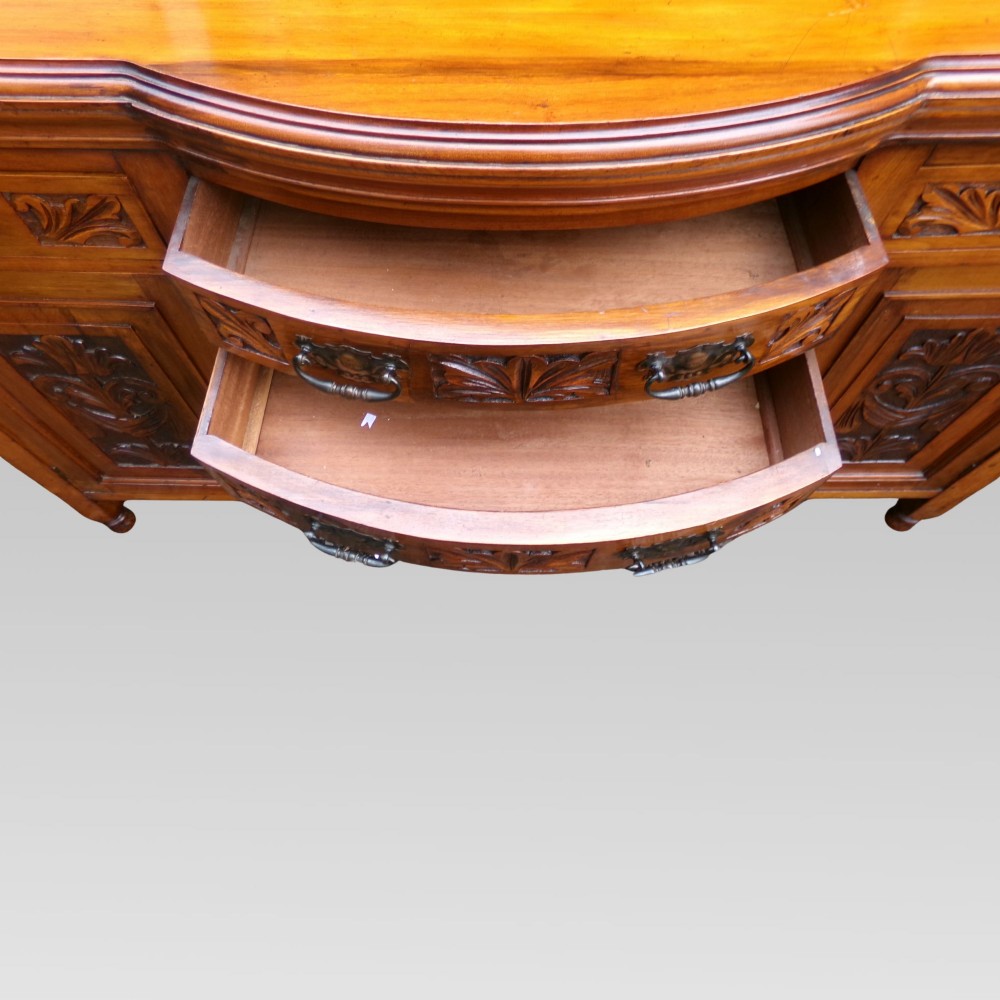 A carved Edwardian mahogany sideboard featuring a bow-front centre section with drawers, flanked by cupboard doors with stylised plant motifs. View VIII