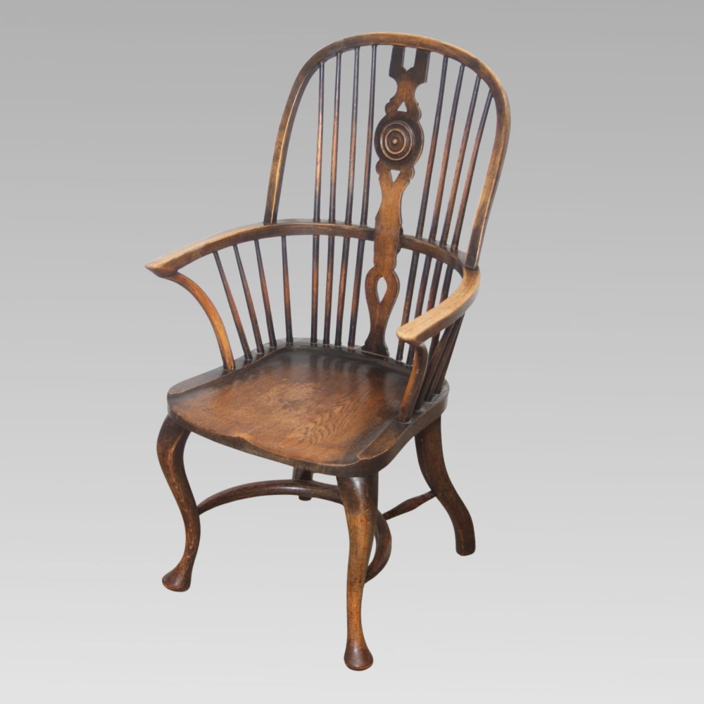 An antique dark oak Windsor armchair featuring a high bowed spindle back, a central carved bullseye splat, cabriole front legs, and a saddled wooden seat.