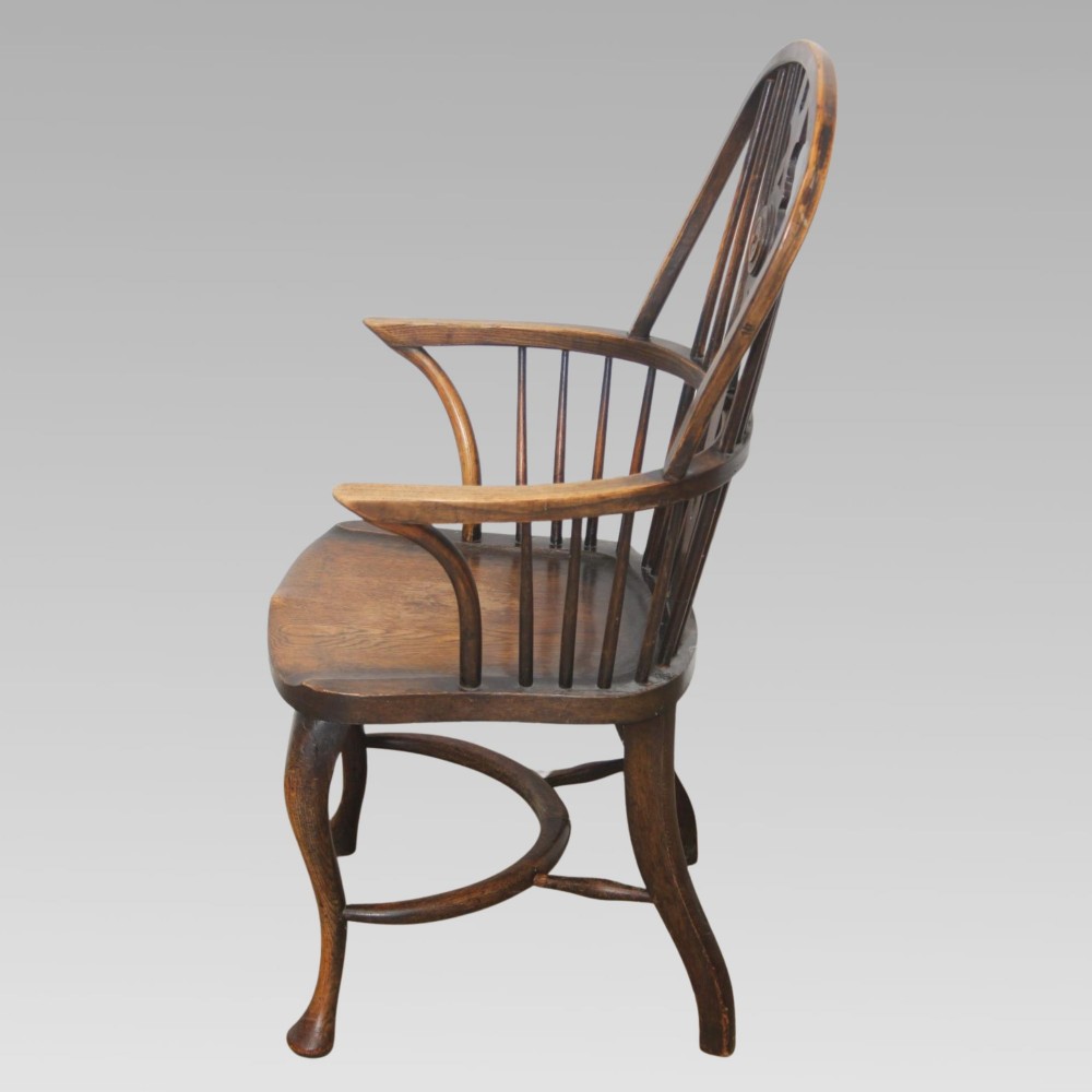 An antique dark oak Windsor armchair featuring a high bowed spindle back, a central carved bullseye splat, cabriole front legs, and a saddled wooden seat. View III