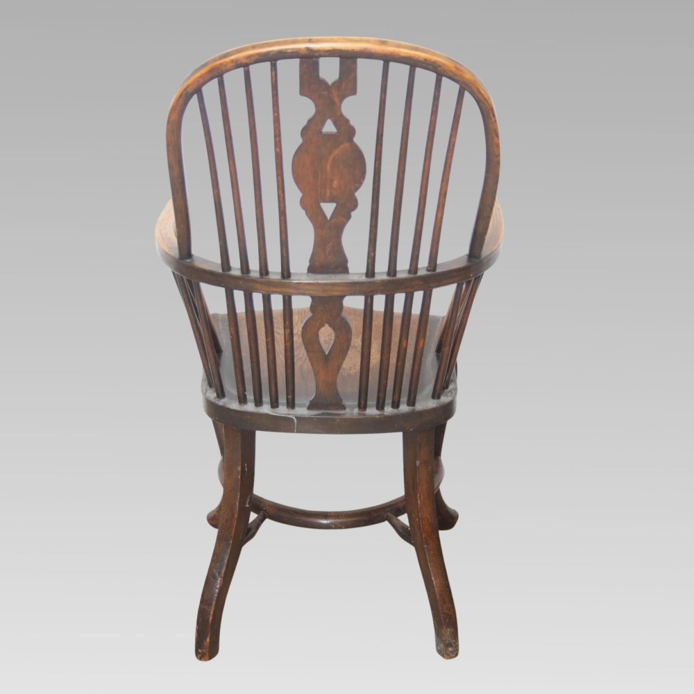 An antique dark oak Windsor armchair featuring a high bowed spindle back, a central carved bullseye splat, cabriole front legs, and a saddled wooden seat. View IV