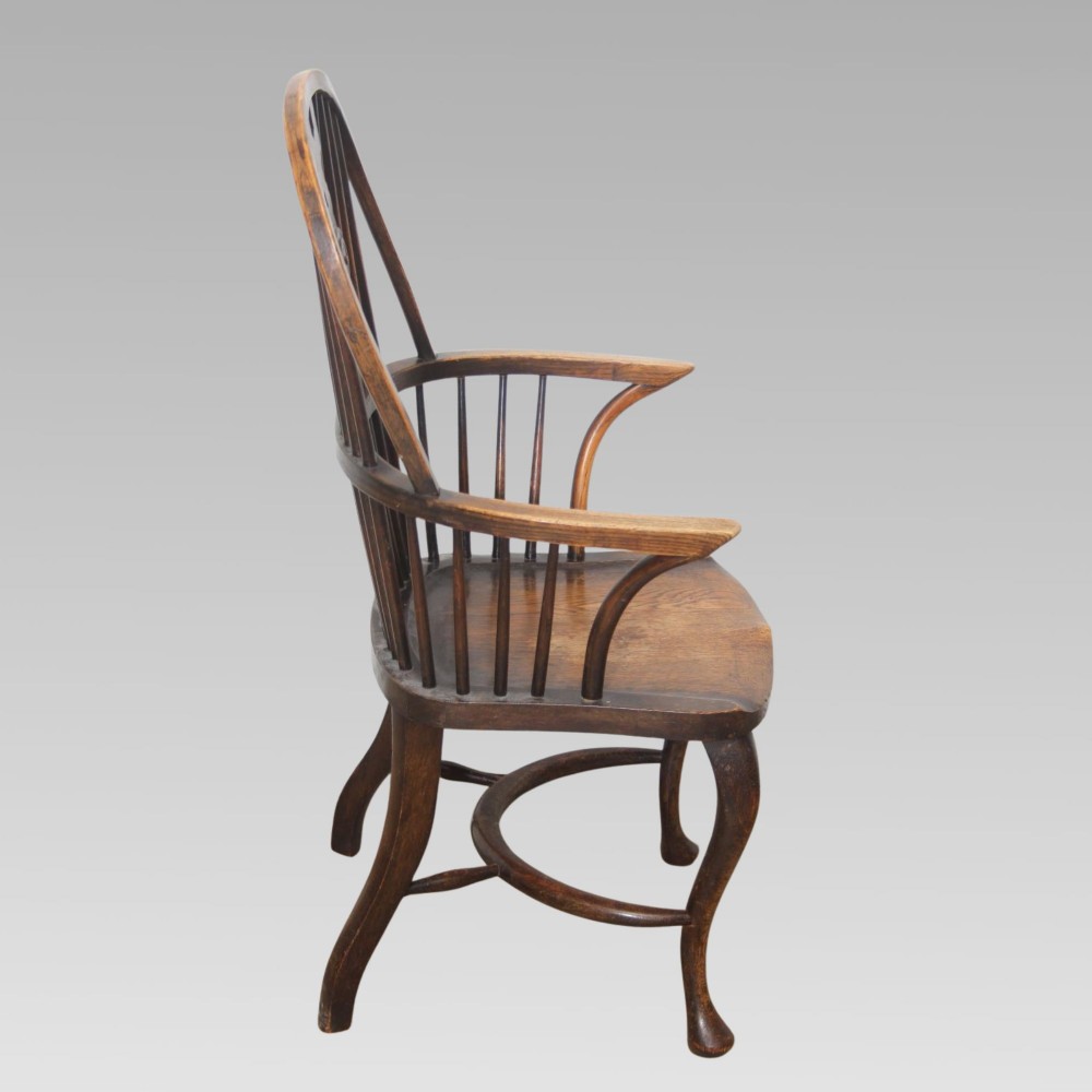 An antique dark oak Windsor armchair featuring a high bowed spindle back, a central carved bullseye splat, cabriole front legs, and a saddled wooden seat. View V