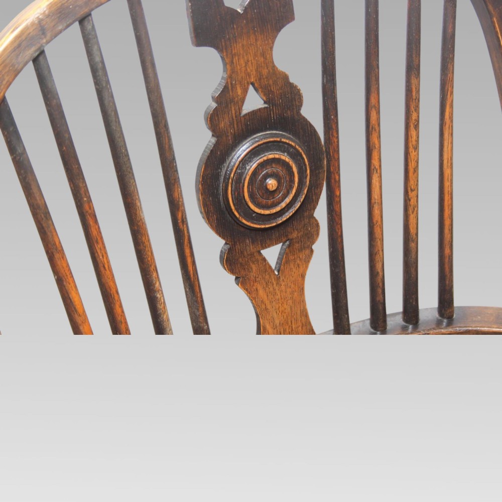 An antique dark oak Windsor armchair featuring a high bowed spindle back, a central carved bullseye splat, cabriole front legs, and a saddled wooden seat. View VI