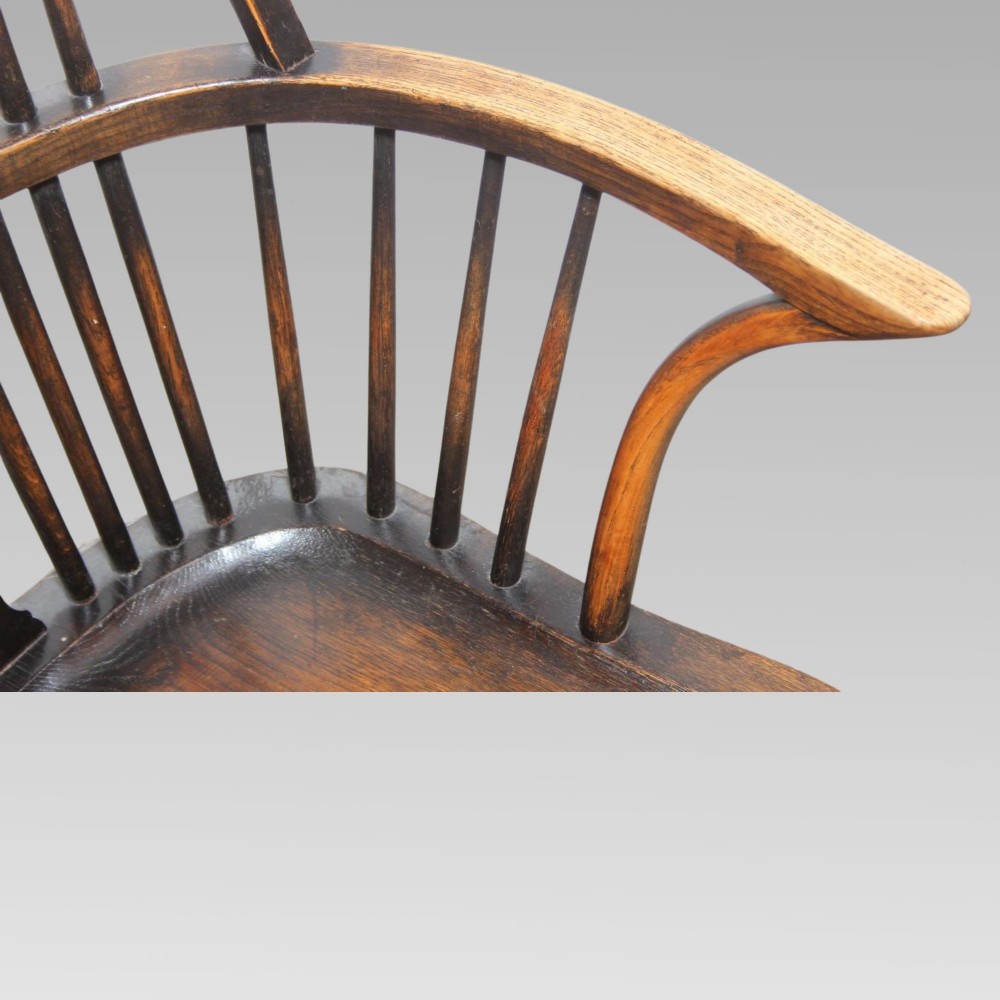 An antique dark oak Windsor armchair featuring a high bowed spindle back, a central carved bullseye splat, cabriole front legs, and a saddled wooden seat. View VII