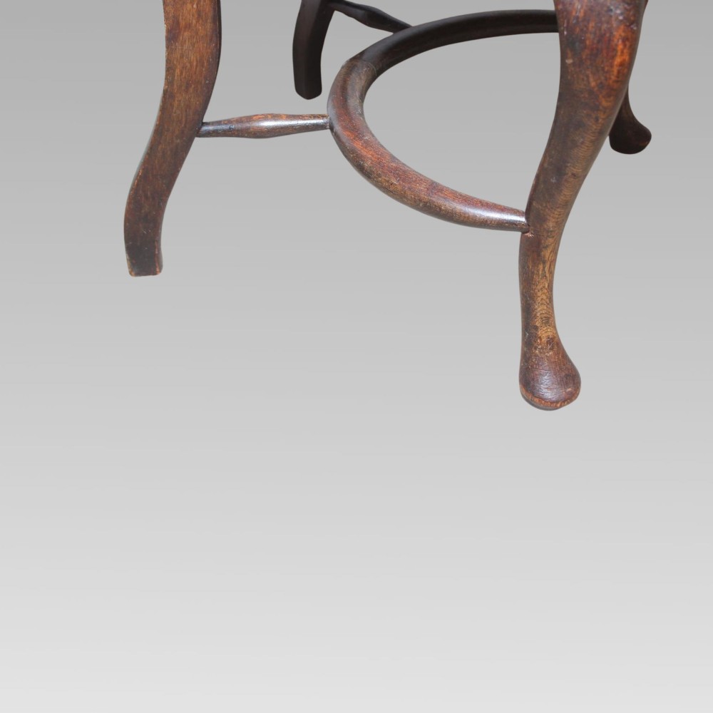 An antique dark oak Windsor armchair featuring a high bowed spindle back, a central carved bullseye splat, cabriole front legs, and a saddled wooden seat. View VIII