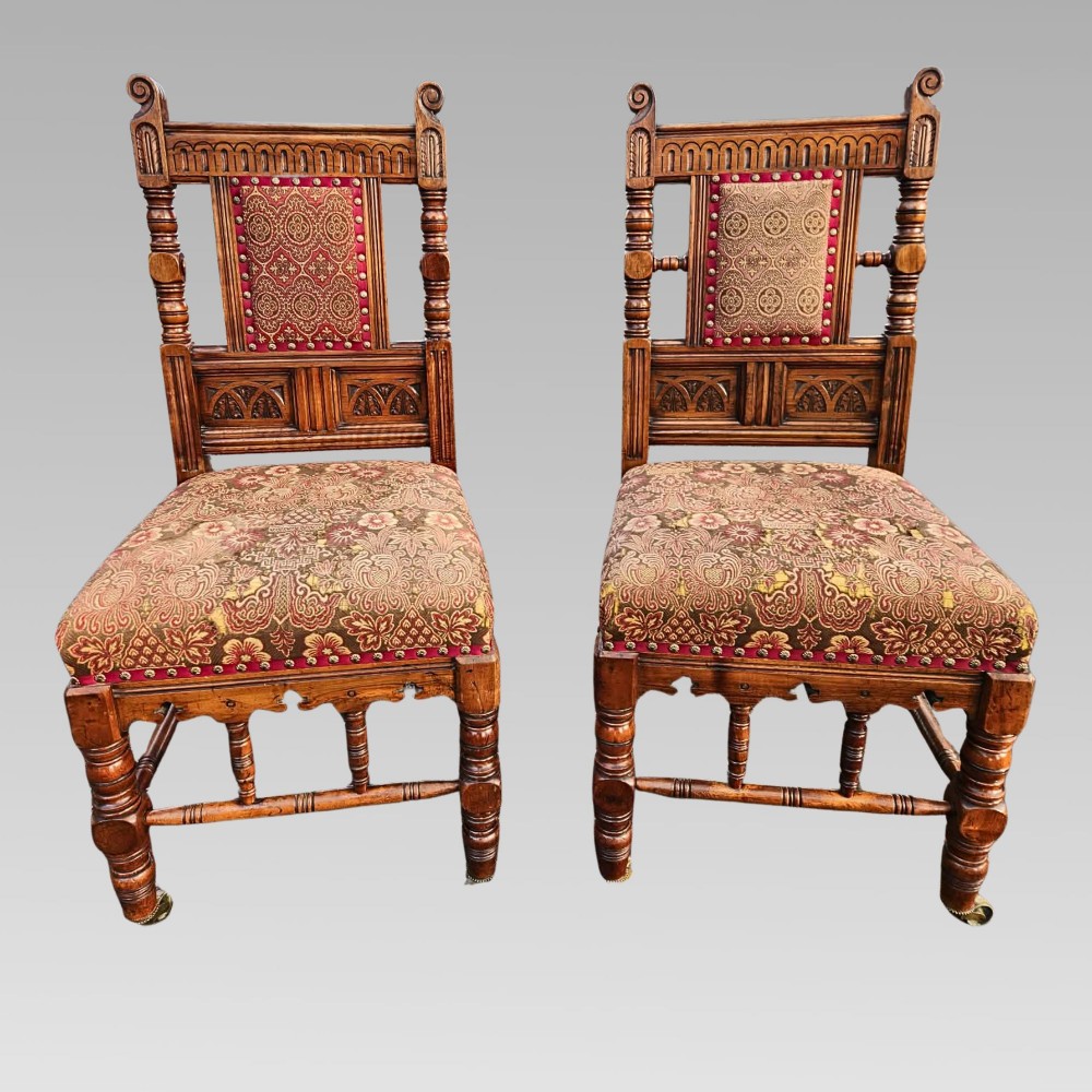 A pair of Victorian Gothic Revival carved oak hall chairs with patterned upholstery and turned legs with brass castors.