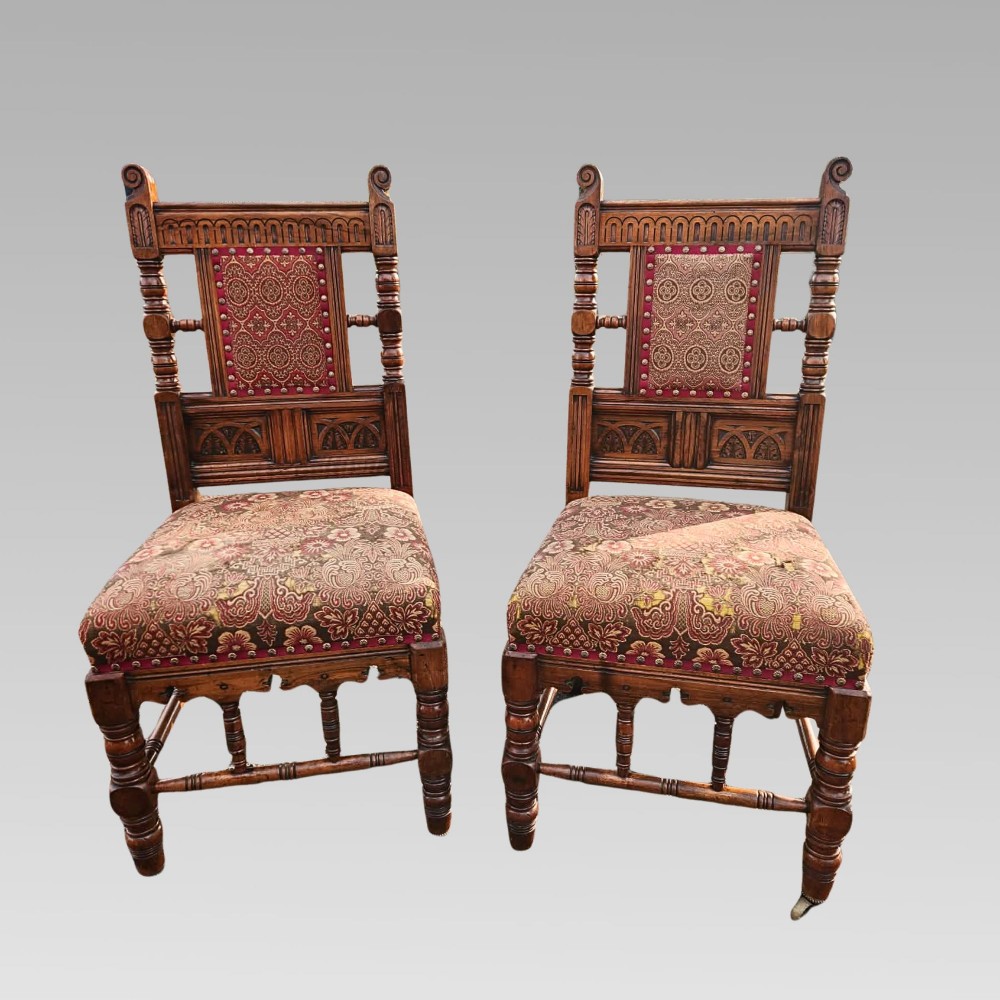 A pair of Victorian Gothic Revival carved oak hall chairs with patterned upholstery and turned legs with brass castors. View II