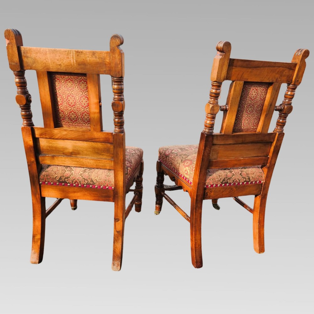 A pair of Victorian Gothic Revival carved oak hall chairs with patterned upholstery and turned legs with brass castors. View III