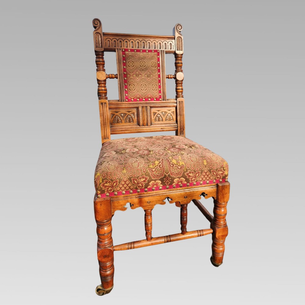 A pair of Victorian Gothic Revival carved oak hall chairs with patterned upholstery and turned legs with brass castors. View IV