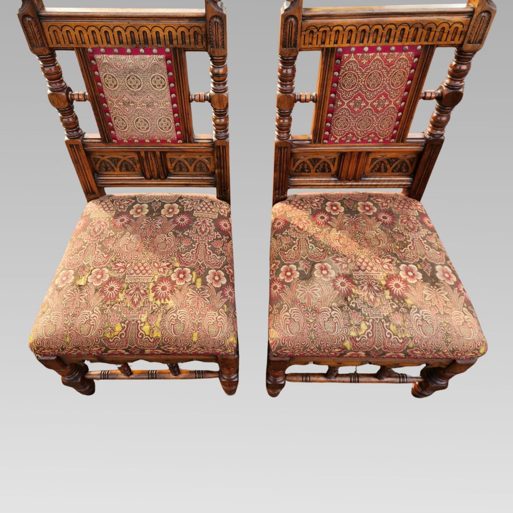 A pair of Victorian Gothic Revival carved oak hall chairs with patterned upholstery and turned legs with brass castors. View V