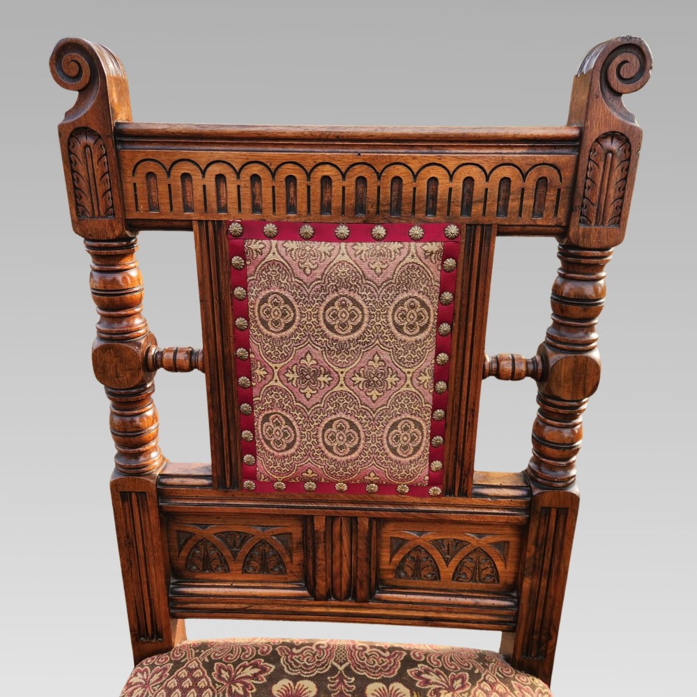 A pair of Victorian Gothic Revival carved oak hall chairs with patterned upholstery and turned legs with brass castors. View VII