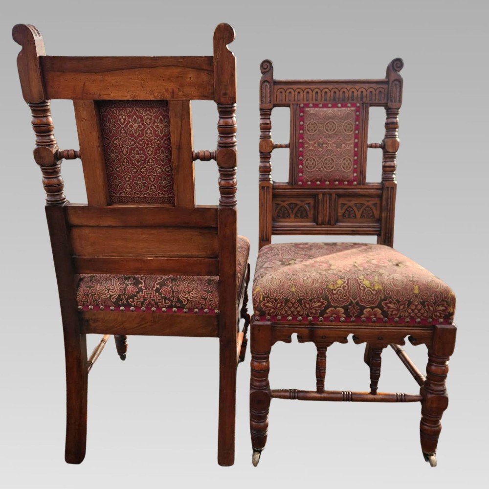 A pair of Victorian Gothic Revival carved oak hall chairs with patterned upholstery and turned legs with brass castors. View IX