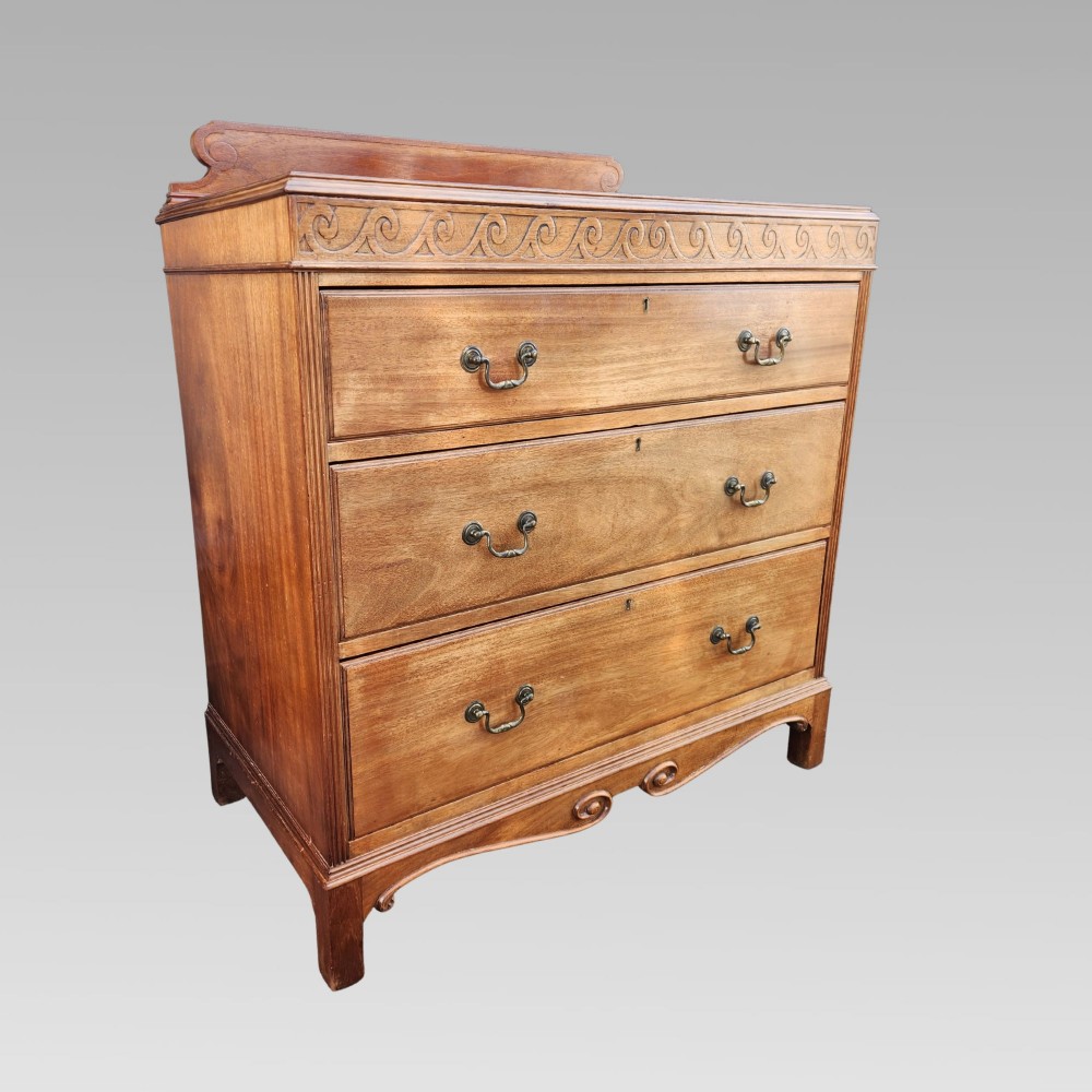 A Victorian mahogany chest of drawers featuring three horizontal drawers with brass handles, a carved wave frieze, and a shaped apron base.