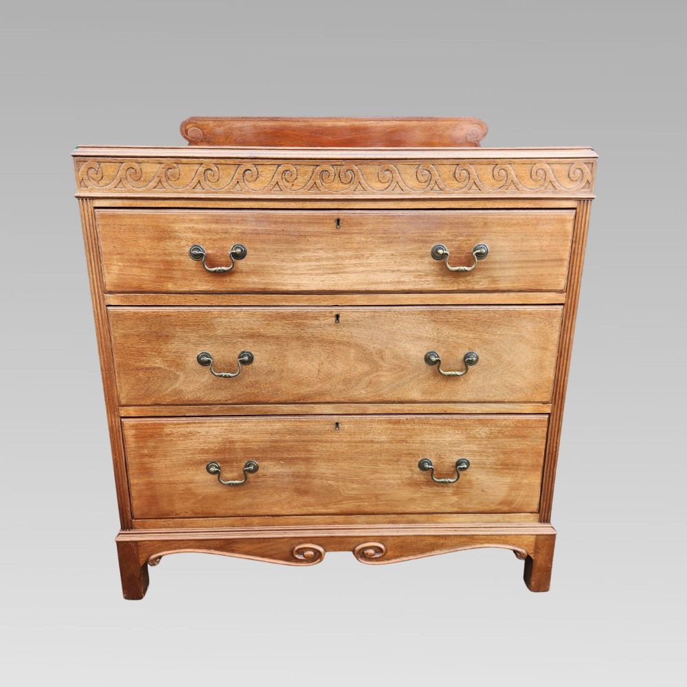 A Victorian mahogany chest of drawers featuring three horizontal drawers with brass handles, a carved wave frieze, and a shaped apron base. View II