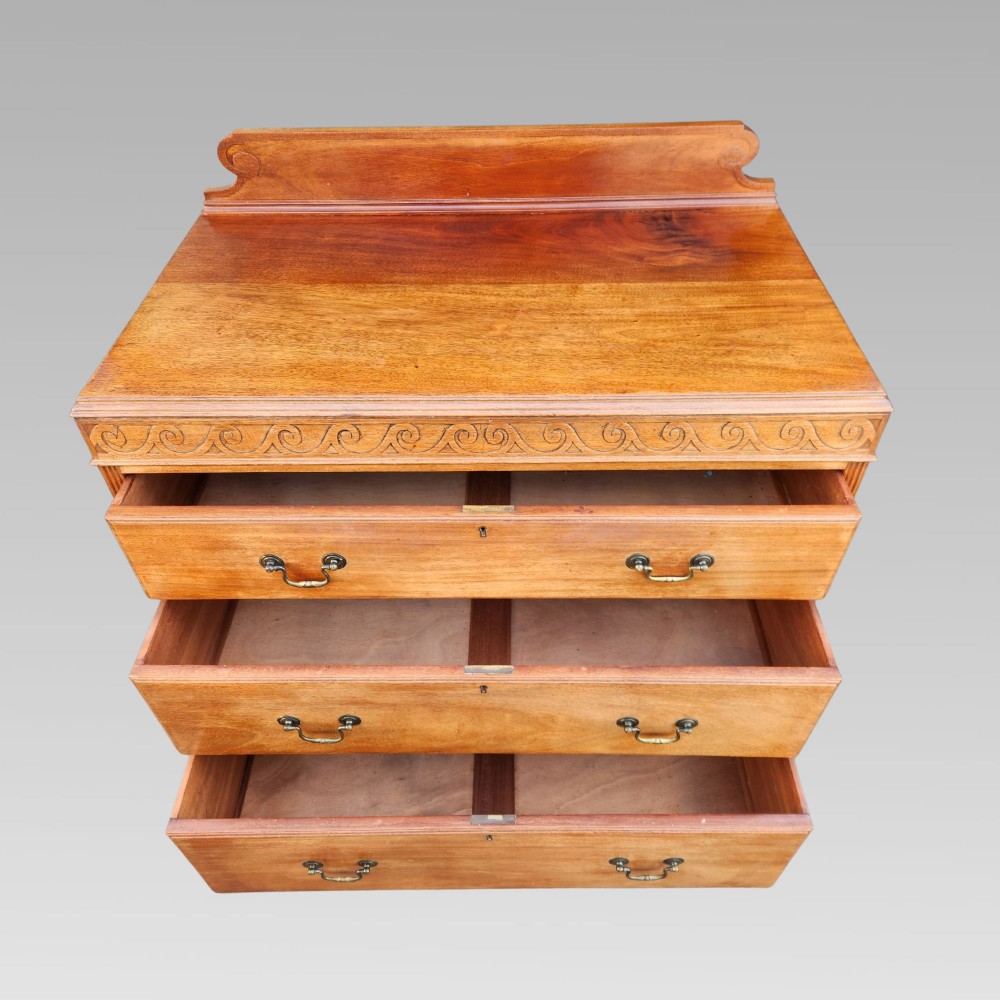 A Victorian mahogany chest of drawers featuring three horizontal drawers with brass handles, a carved wave frieze, and a shaped apron base. View III