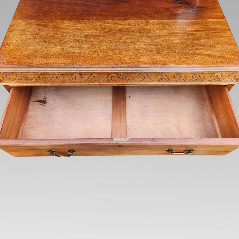 A Victorian mahogany chest of drawers featuring three horizontal drawers with brass handles, a carved wave frieze, and a shaped apron base. View VI