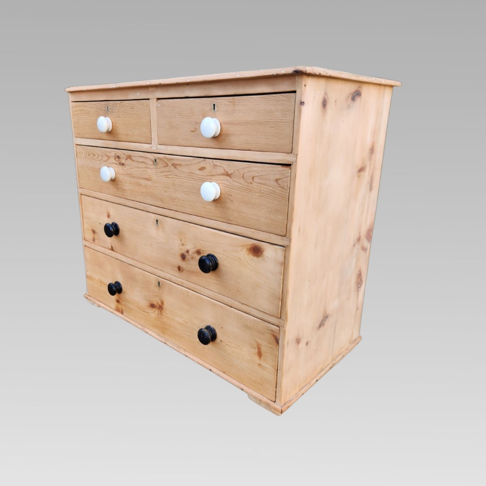 A 19th-century Victorian pine chest of drawers featuring two short over three long drawers with turned white ceramic and black wooden knobs.