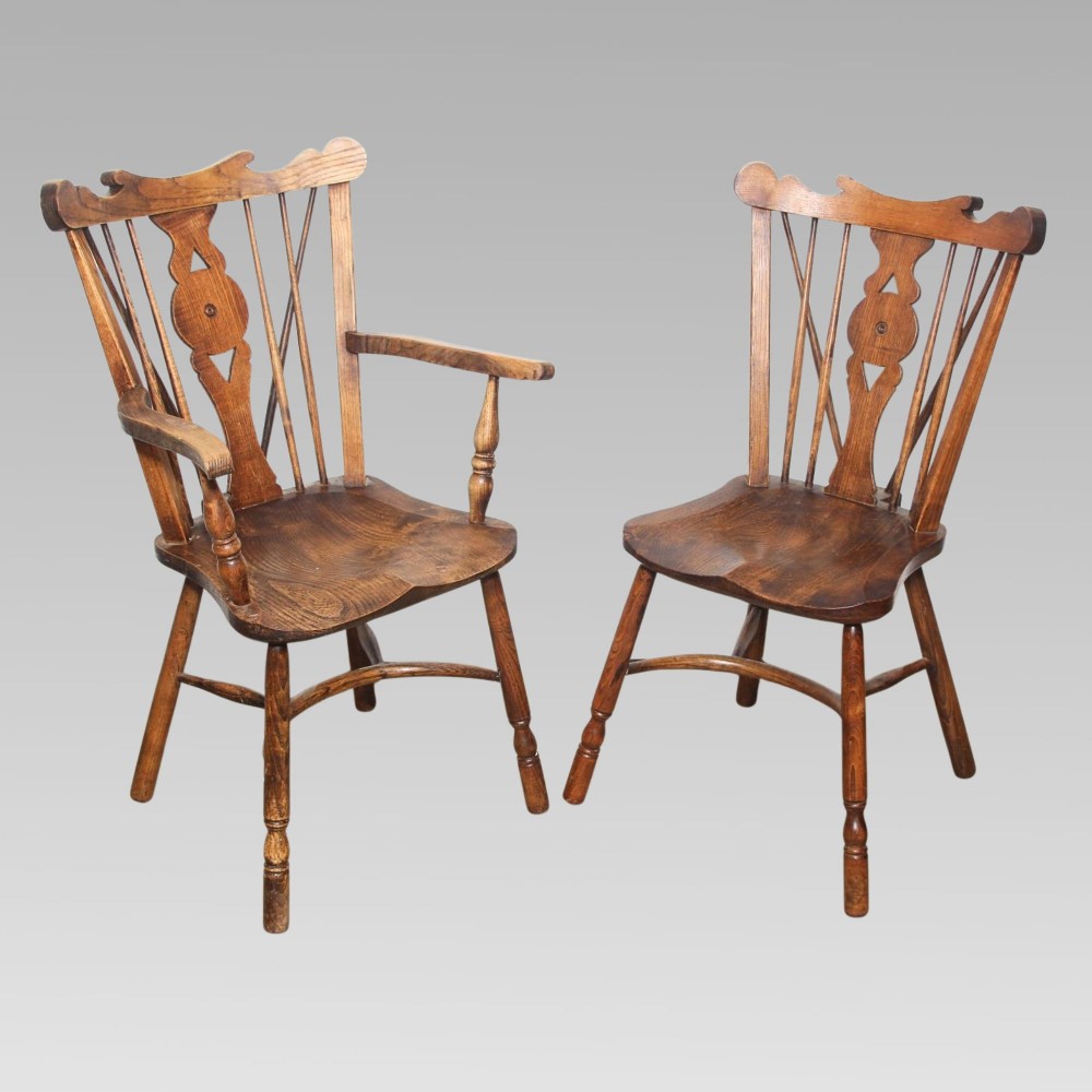 A pair of antique warm brown elm Thames Valley Windsor chairs featuring stick backs, central decorative splats, turned legs, and shaped seats.