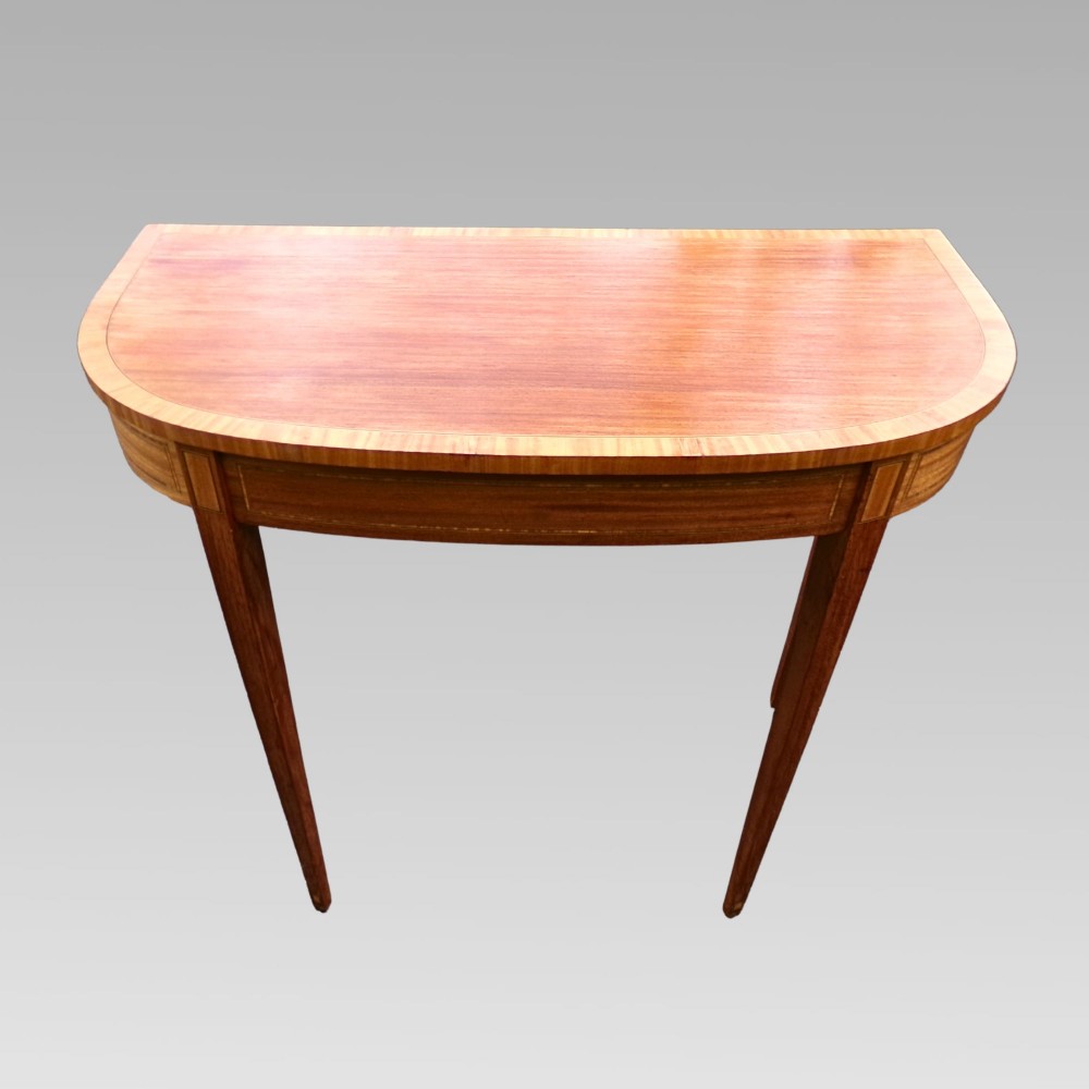 A Georgian style semicircular satinwood console table featuring crossbanded veneer borders and square tapered legs.