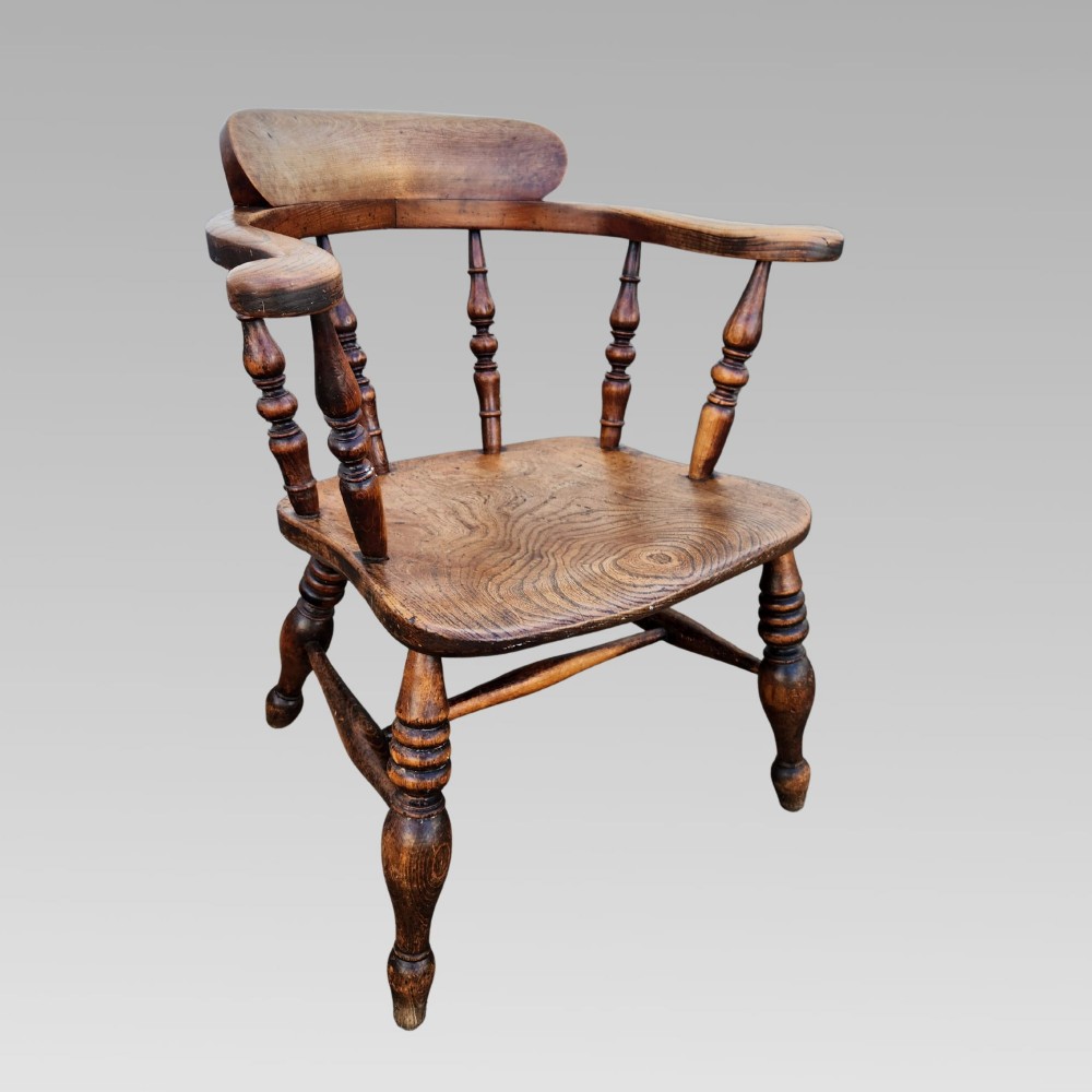 A nineteenth-century turned wood smokers bow armchair featuring a shaped elm seat and turned beech spindles.