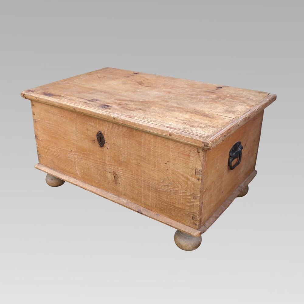 A rectangular nineteenth-century pine blanket box with turned bun feet, side iron drop handles, and a central keyhole escutcheon.