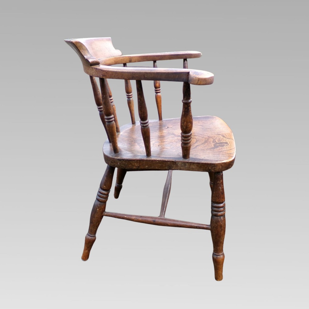 A nineteenth-century elm and beech smokers bow captains armchair featuring turned legs, vertical spindles, and a shaped seat. View V
