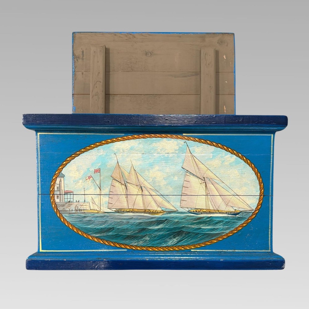 A blue painted wooden storage box featuring a hand-painted scene of sailing yachts and lettering reading The Yacht Britannia Cowes I.O.W. 1902. View IV