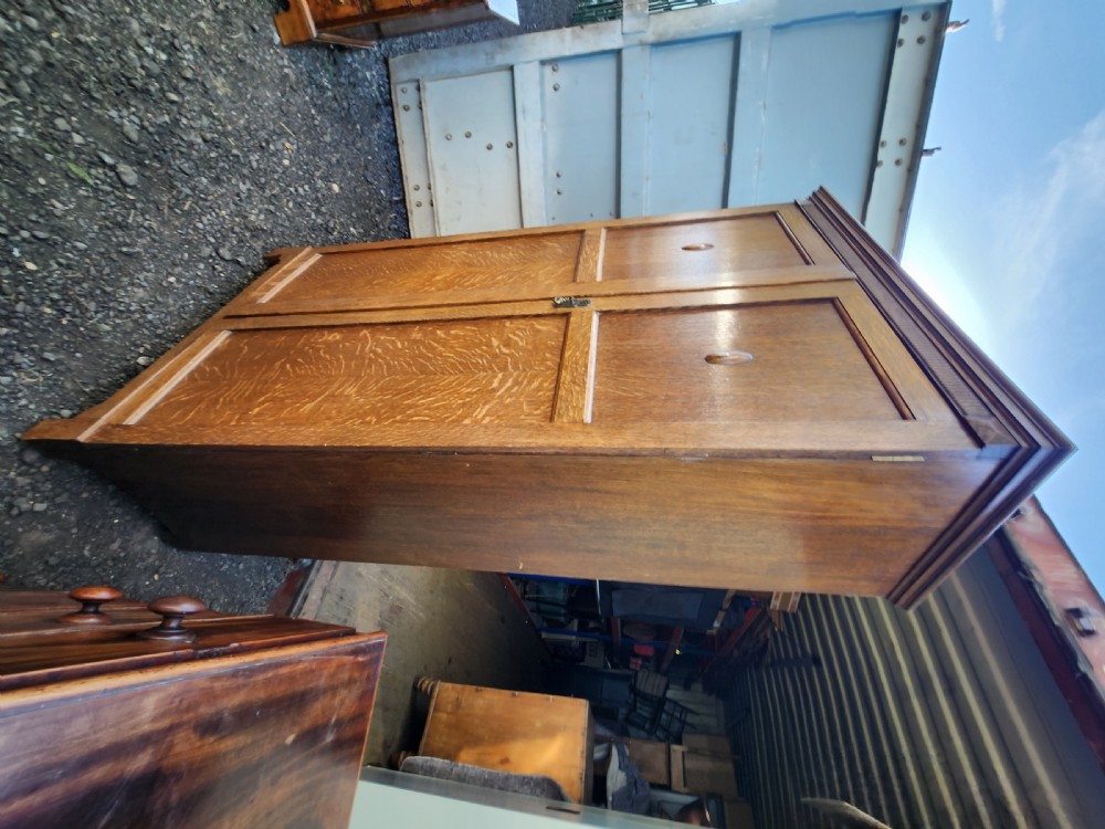A tall 1920s limed oak gentlemans wardrobe featuring twin panelled doors with oval carved handles and a fluted top cornice. View III
