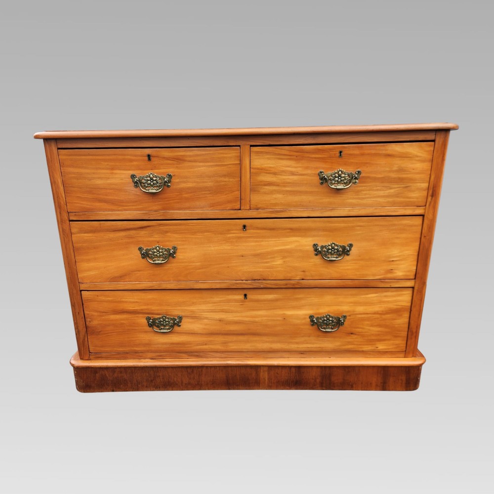 An antique Edwardian satinwood chest of drawers featuring two short upper drawers, two long lower drawers, brass drop handles with decorative backplates, and a plinth base.