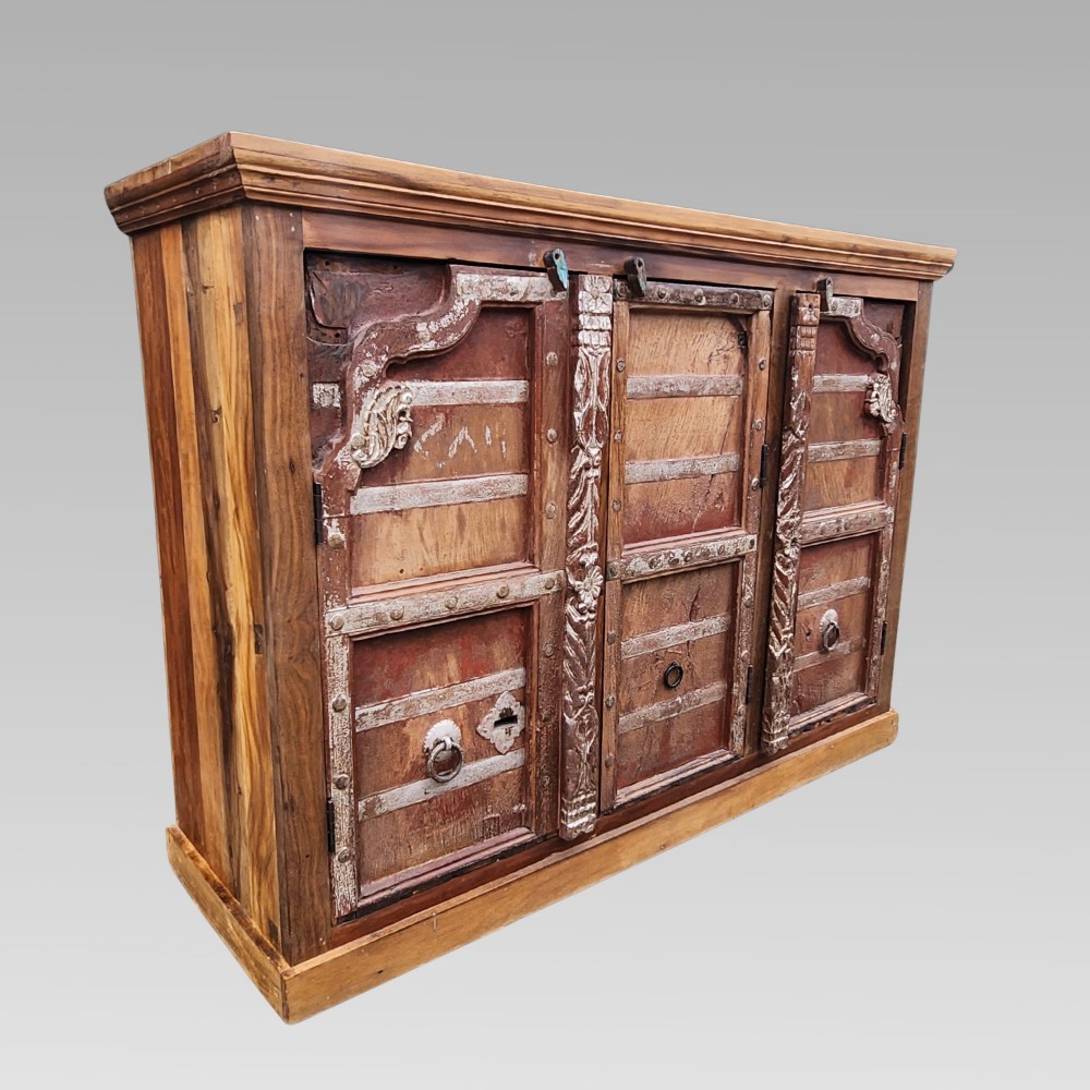A rustic three-door reclaimed teak sideboard featuring hand-carved floral pilasters, iron ring handles, and metal stud accents.