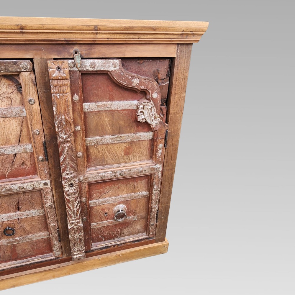 A rustic three-door reclaimed teak sideboard featuring hand-carved floral pilasters, iron ring handles, and metal stud accents. View VI
