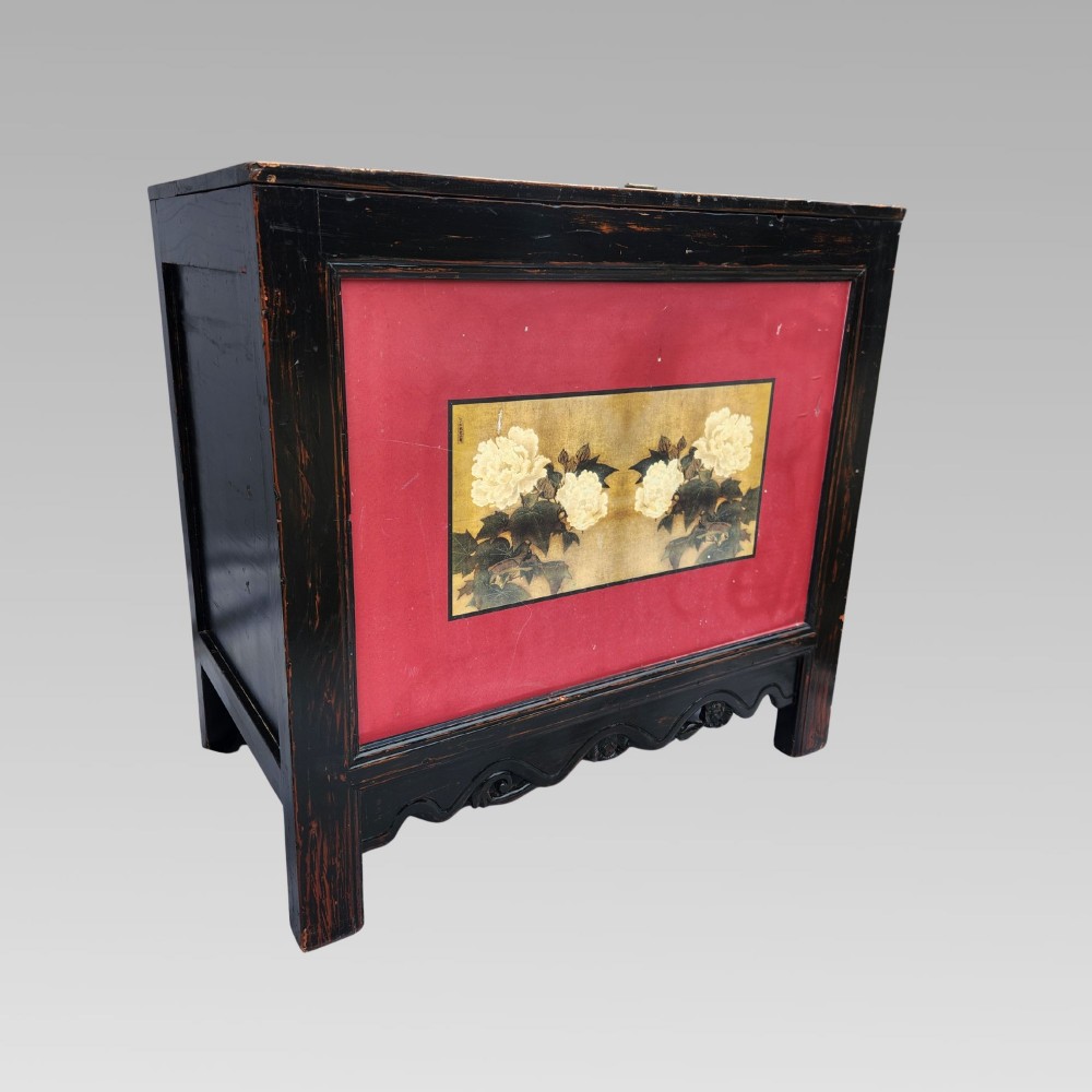 A dark lacquered wooden storage chest featuring a framed red panel with a hand-painted floral image of white peonies on a gold background.
