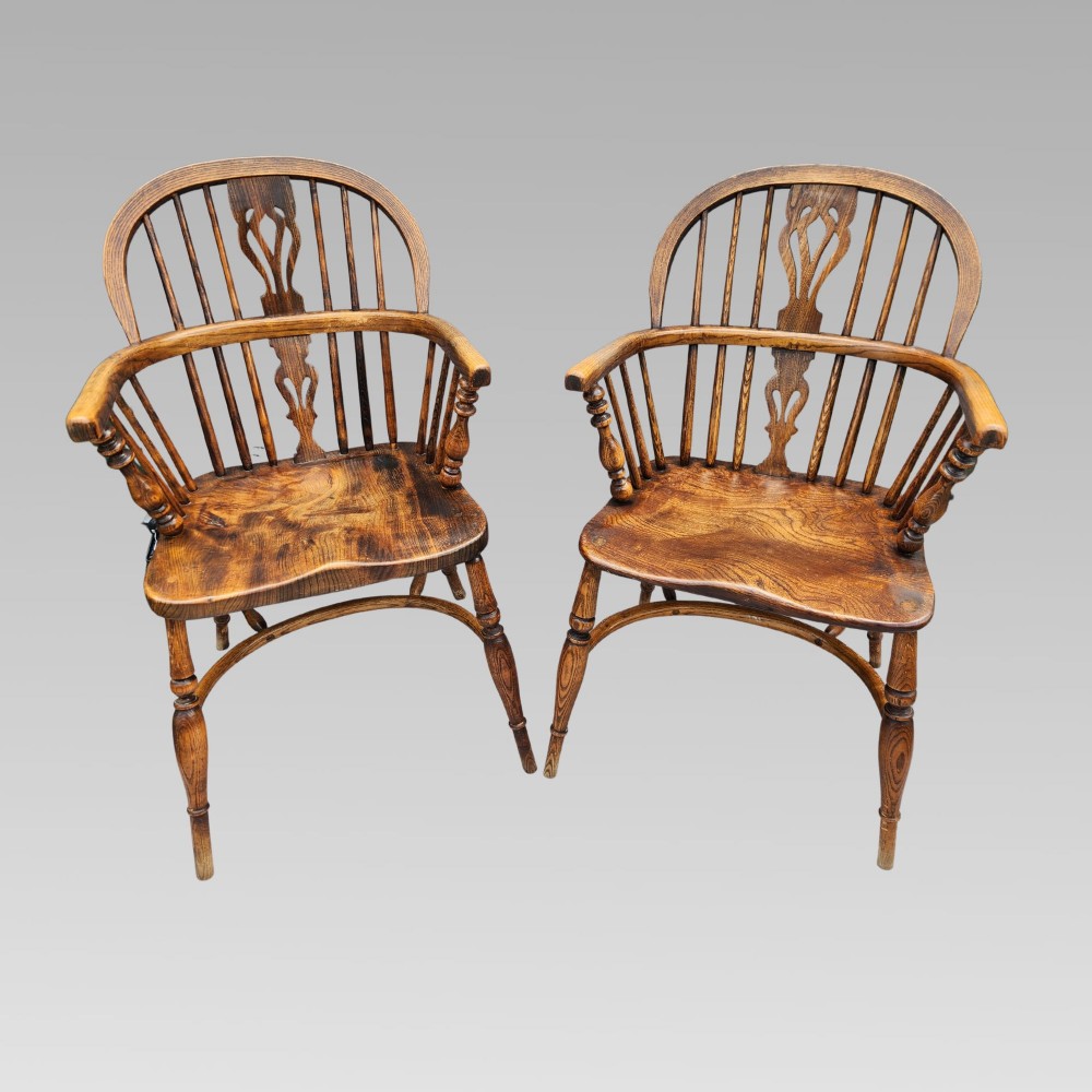 A pair of antique wooden Windsor armchairs featuring shaped elm seats, spindle backs with pierced central splats, and curved crinoline stretchers.
