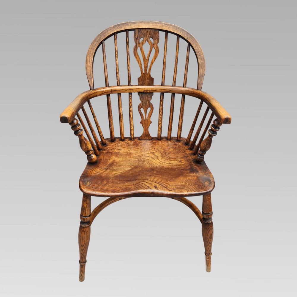 An antique elm Windsor armchair featuring a hoop back, a pierced splat, turned legs, and a curved crinoline stretcher. View II