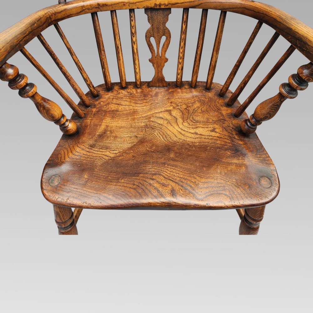 An antique elm Windsor armchair featuring a hoop back, a pierced splat, turned legs, and a curved crinoline stretcher. View III
