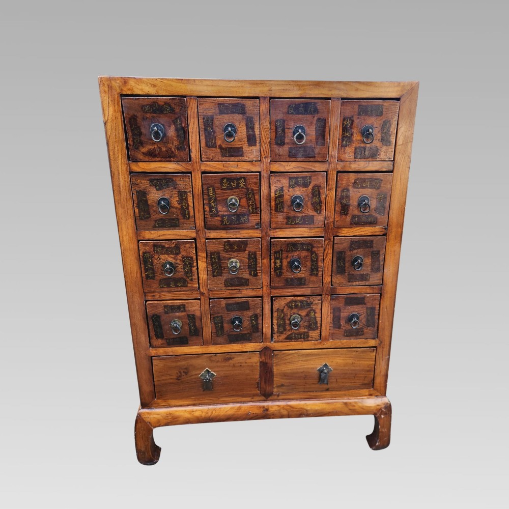 A tall warm brown elm apothecary chest featuring sixteen small labelled drawers above two wider base drawers with metal ring pulls. View III