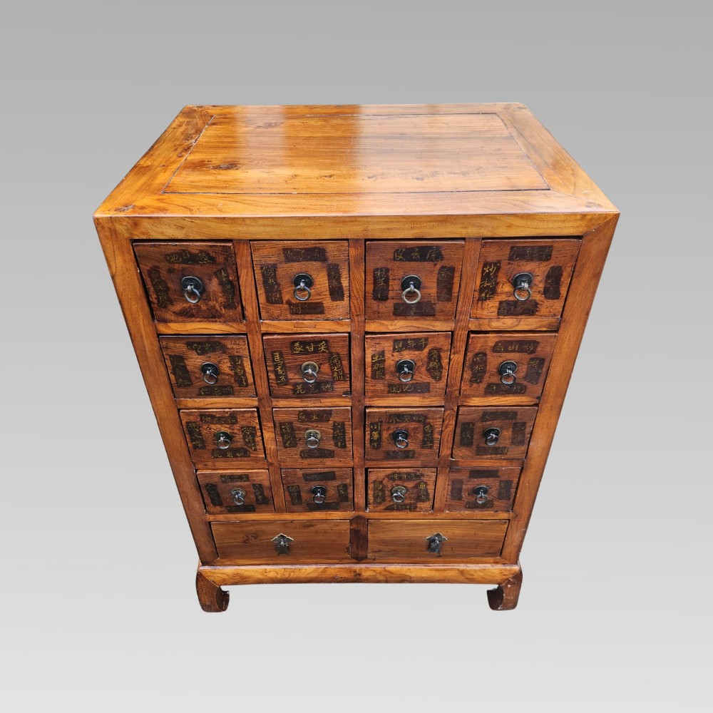A tall warm brown elm apothecary chest featuring sixteen small labelled drawers above two wider base drawers with metal ring pulls. View IX
