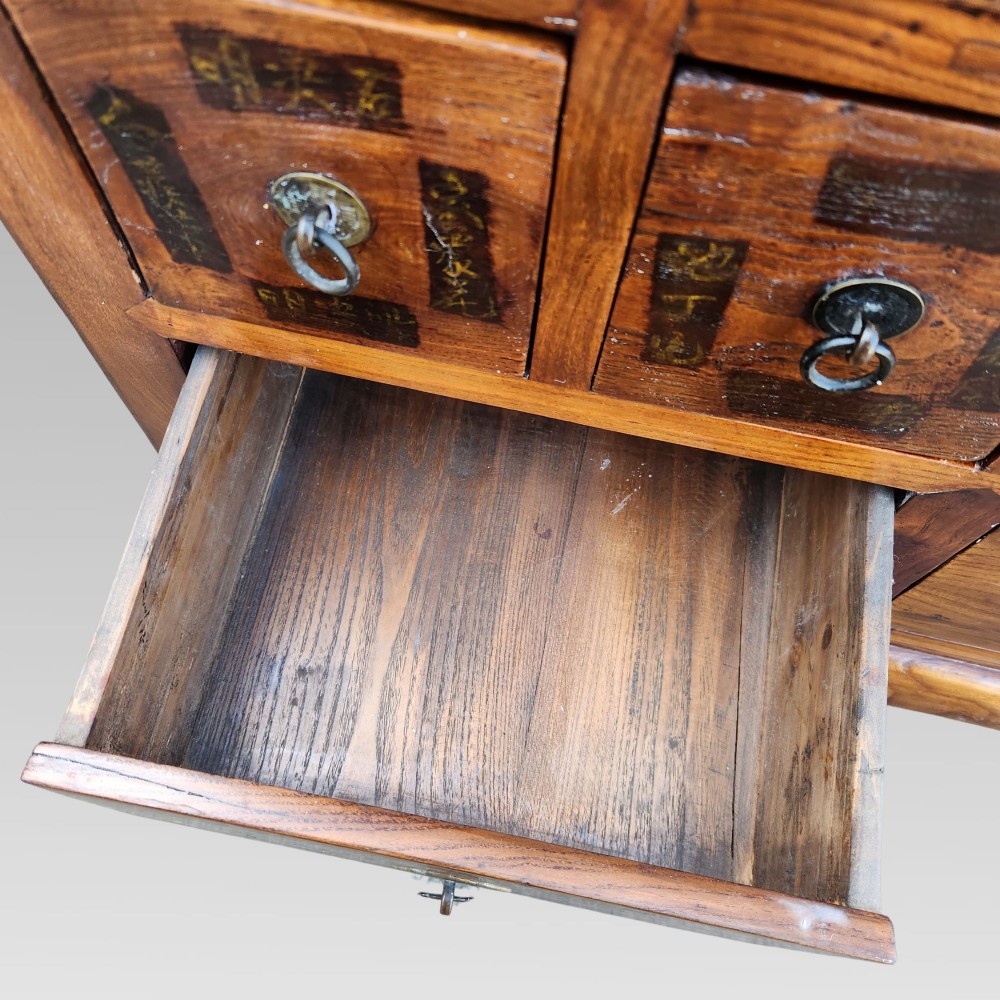 A tall warm brown elm apothecary chest featuring sixteen small labelled drawers above two wider base drawers with metal ring pulls. View X