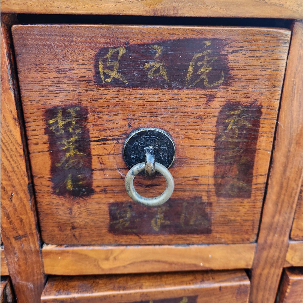 A tall warm brown elm apothecary chest featuring sixteen small labelled drawers above two wider base drawers with metal ring pulls. View XIII