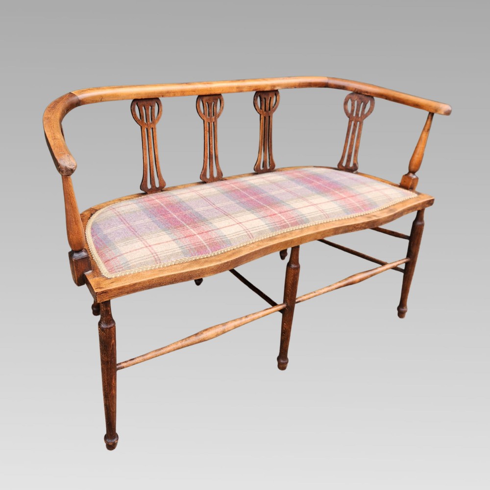 An Edwardian wooden salon settee featuring a curved armrail, pierced splats, turned legs, and a pastel tartan upholstered seat. View II
