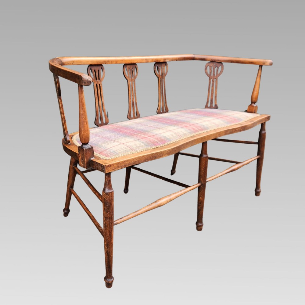 An Edwardian wooden salon settee featuring a curved armrail, pierced splats, turned legs, and a pastel tartan upholstered seat. View III