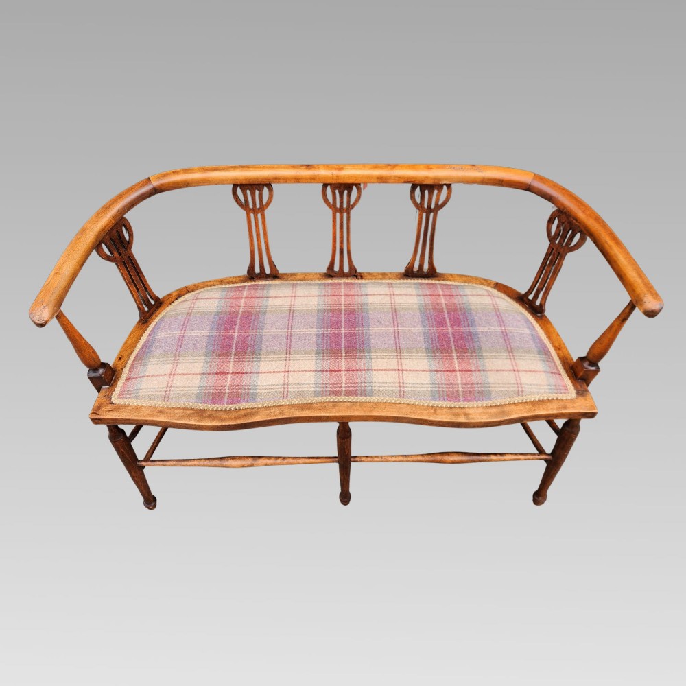 An Edwardian wooden salon settee featuring a curved armrail, pierced splats, turned legs, and a pastel tartan upholstered seat. View IV