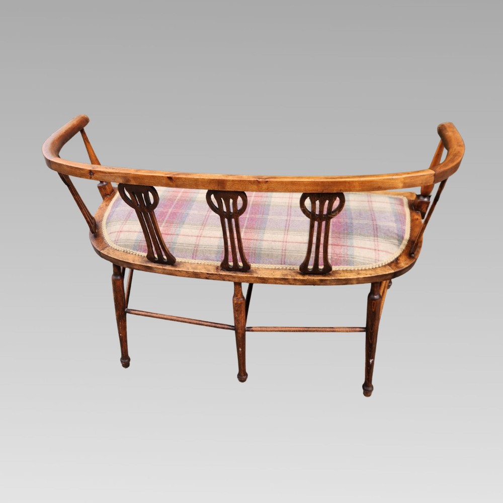 An Edwardian wooden salon settee featuring a curved armrail, pierced splats, turned legs, and a pastel tartan upholstered seat. View VI