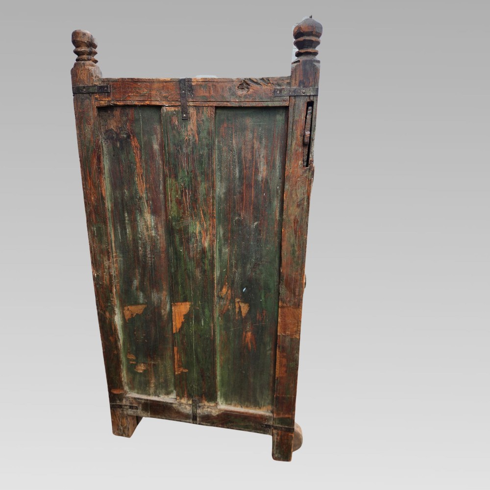 A rustic wooden Indian almirah storage cupboard with distressed green paint, double panel doors, iron fittings, turned corner finials, and wooden wheels. View VIII