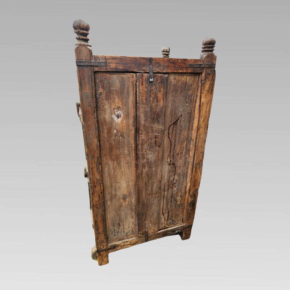 A rustic wooden Indian almirah storage cupboard with distressed green paint, double panel doors, iron fittings, turned corner finials, and wooden wheels. View IX