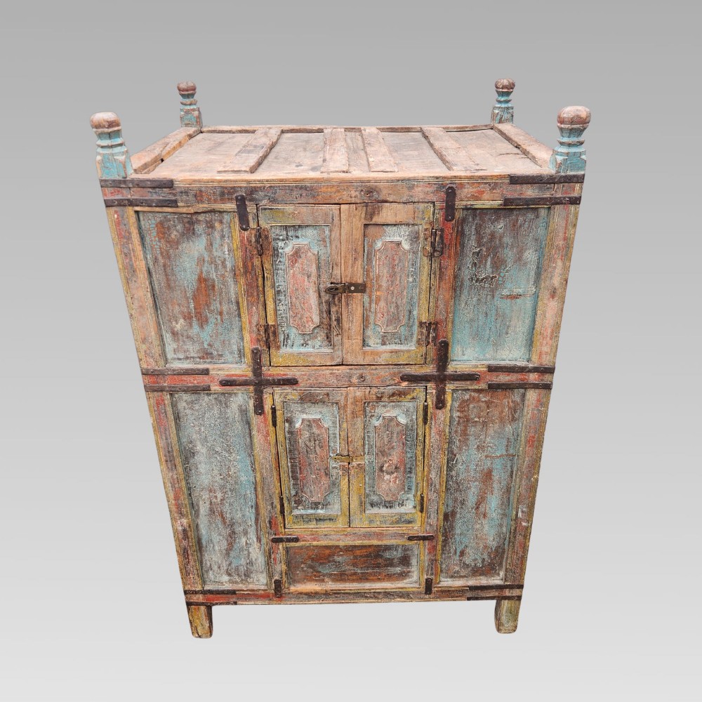A tall antique Indian wooden almirah cabinet featuring layered distressed blue paint, iron strapping, panelled doors, and corner finials. View II