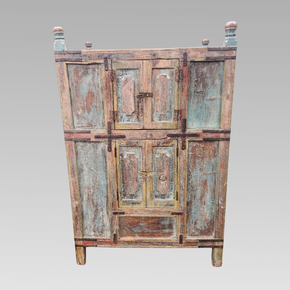 A tall antique Indian wooden almirah cabinet featuring layered distressed blue paint, iron strapping, panelled doors, and corner finials. View IV