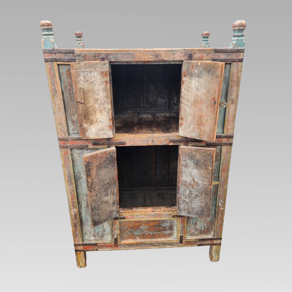 A tall antique Indian wooden almirah cabinet featuring layered distressed blue paint, iron strapping, panelled doors, and corner finials. View VI
