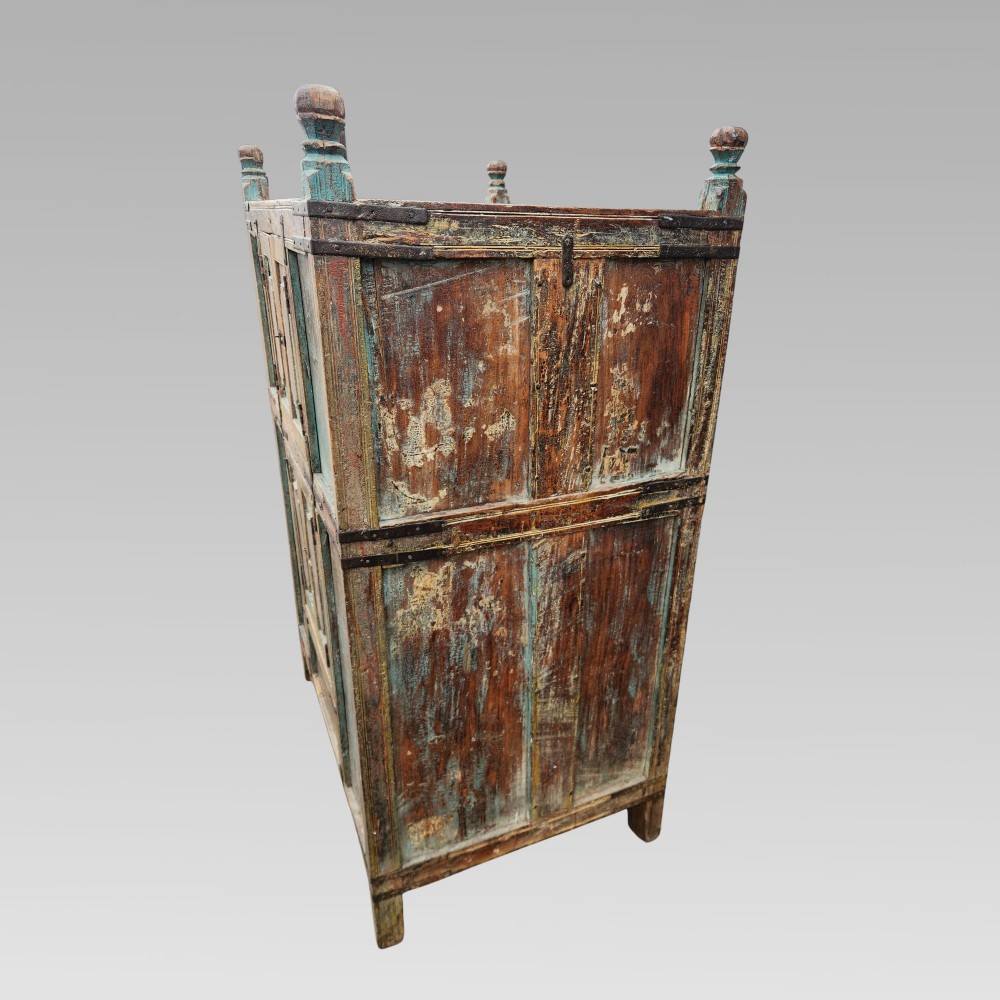 A tall antique Indian wooden almirah cabinet featuring layered distressed blue paint, iron strapping, panelled doors, and corner finials. View IX