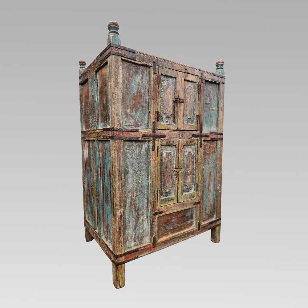A tall antique Indian wooden almirah cabinet featuring layered distressed blue paint, iron strapping, panelled doors, and corner finials. View XI